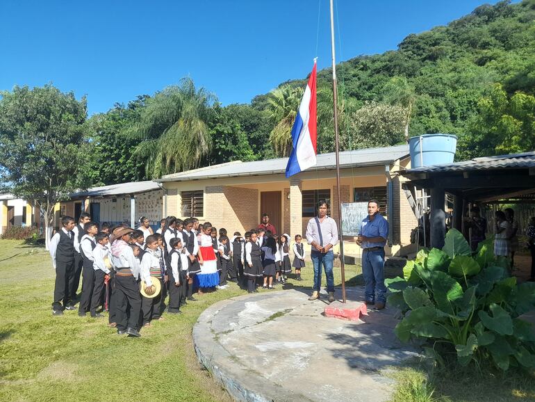 Izamiento del pabellón patrio a cargo del intendente y el líder de la comunidad, en presencia de alumnos de la escuela.