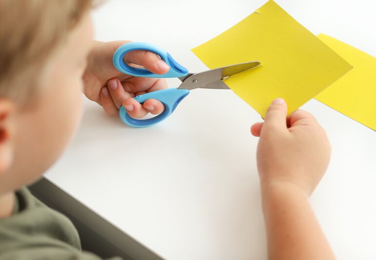 Un niño zurdo corta un pedazo de papel.