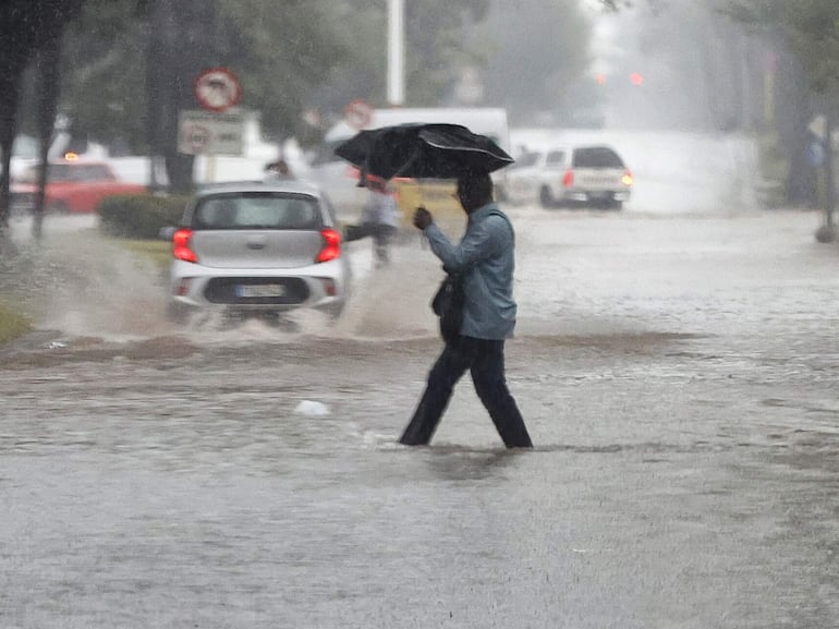 Imagen ilustrativa: un hombre intenta protegerse de la lluvia con un paraguas. 
