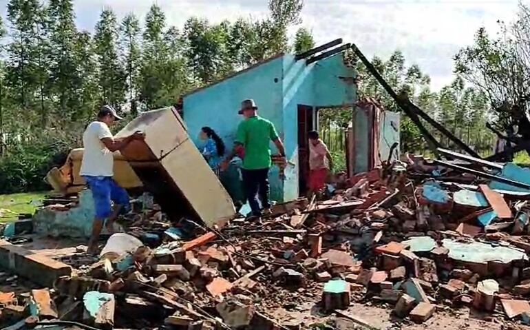 Una casa derrumbada. Solo queda una porción de la edificación en pie, mientras que el suelo está lleno de escombros y ladrillos. Una persona retira una heladera y otras personas caminan sobre las ruinas.