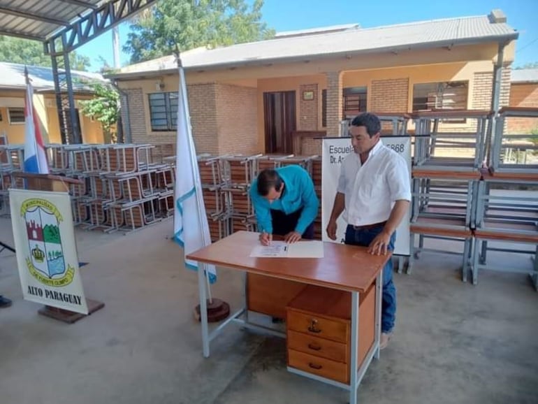 El director de la escuela de Toro Pampa, Felix González, firma el documento de recepción de los bienes entregados, a su lado el intendente Moisés Recalde (ANR).