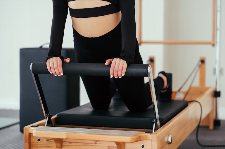 Torso de una mujer agarrada a la barra de un pilates reformer.