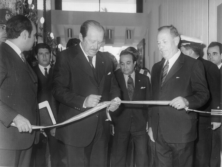 Inauguración del Edificio Monumental, 20 de julio de 1973. El dictador Alfredo Stroessner y el propietario, Jacobo Tauber, cortando la cinta. En segunda fila, el secretario privado del dictador, Mario Abdo Benítez. A la derecha de Stroessner, atajando la cinta, el jefe de protocolo de la presidencia Conrado (Teruco) Pappalardo Zaldívar