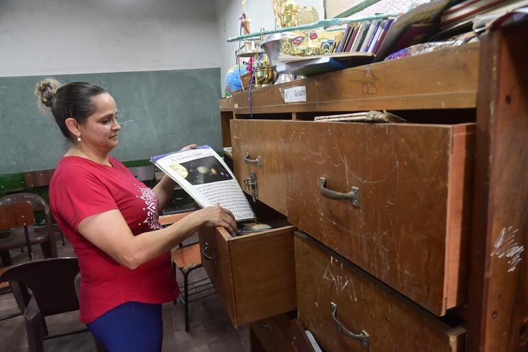 La coordinadora  María Acevedo, de la escuela básica 1.003 del barrio Santa Ana, muestra un libro extraído de un viejo estante. El mueble es lo que queda de la biblioteca de la institución educativa.