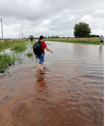 Una docente cruza a pie en la zona de Tacuara´i del distrito de Tacuaras para llegar a la ruta PY04 luego de que el vehículo que lo transportaba quedara atascado en el camino en medio del agua.