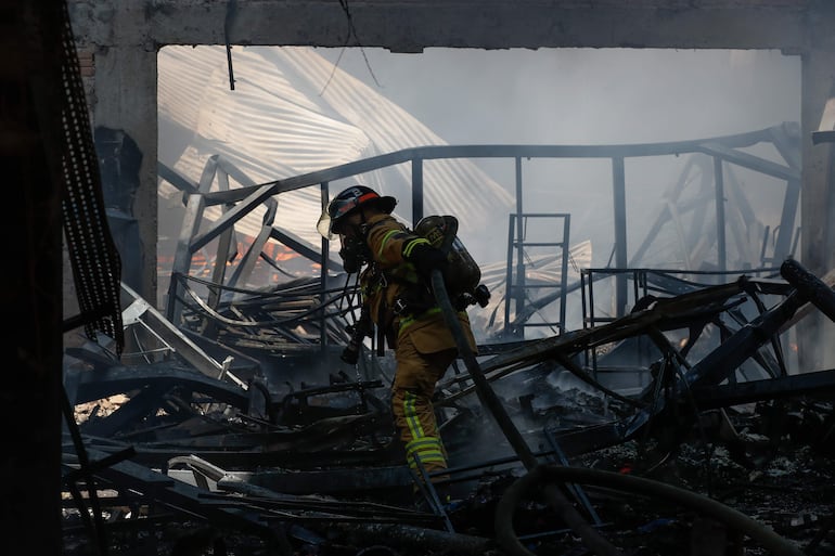 Un bombero voluntario controla un incendio de gran magnitud en un depósito de ropa deportiva este lunes, en la ciudad de Fernando de la Mora (Paraguay). EFE/ Juan Pablo Pino