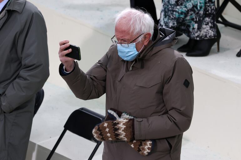 Una selfie pa'l Facebook, parece pensar Bernie mientras se enfoca a sí mismo durante el acto de asunción al mando de Joe Biden. 