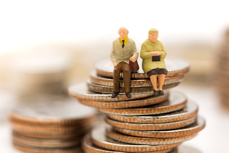 Dos figuras que representan a una pareja de adultos mayores sentados sobre una pila de monedas.