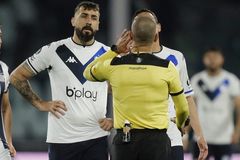 El árbitro paraguayo Eber Aquino escucha a los asistentes del VAR durante el partido de vuelta argentino de cuartos de final del torneo de fútbol Copa Libertadores entre Talleres de Córdoba y Vélez Sarsfield, en el estadio Mario Kempes de Córdoba, Argentina, el 10 de agosto de 2022.
