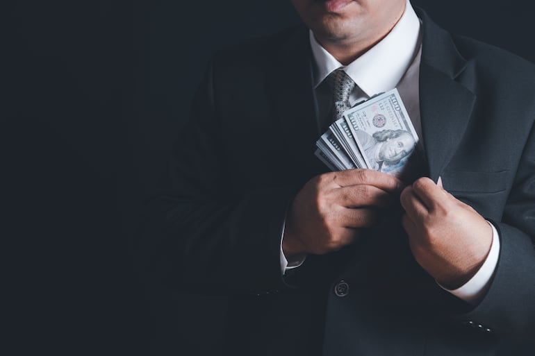 Un hombre guarda billetes de dólares en el bolsillo interno de su saco.