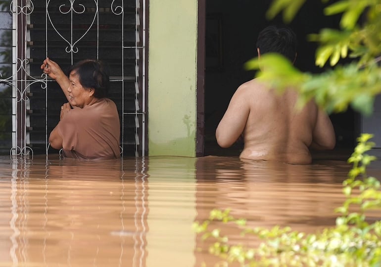 El agua tapa la mitad del cuerpo de dos vecinos que tratan de acceder a su vivienda en una zona de la provincia de Chiang Rai, en el norte de Tailandia.