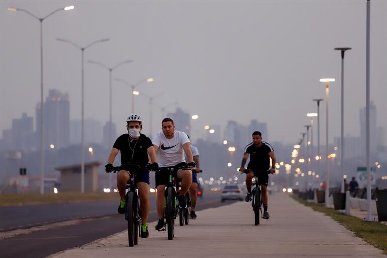 Ciclistas se desplazan en bicicleta en medio del humo en la Costanera de Asunción.