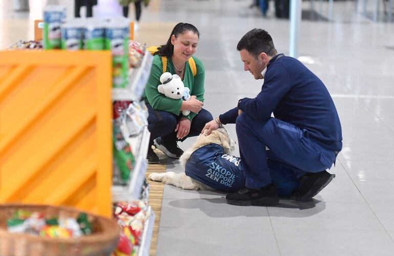 Un hombre juega y acaricia a Dino, un golden retriever guiado por su entrenadora Vesna Kiskovska (izq.), en el Aeropuerto Internacional de Skopie.