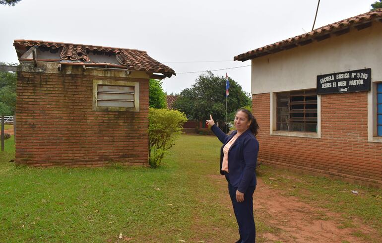 La encargada de despacho de la institución, Rosa Martínez, señalando el baño que está practicamente destruido.