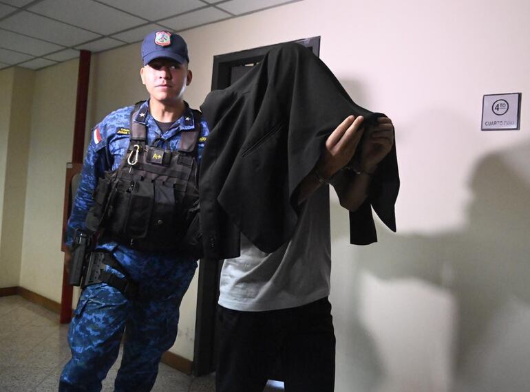 El oficial segundo Hugo Javier Vallejos Rivas sale esposado y con el rostro cubierto de la audiencia de imposición de medidas en el Palacio de Justicia de Asunción.