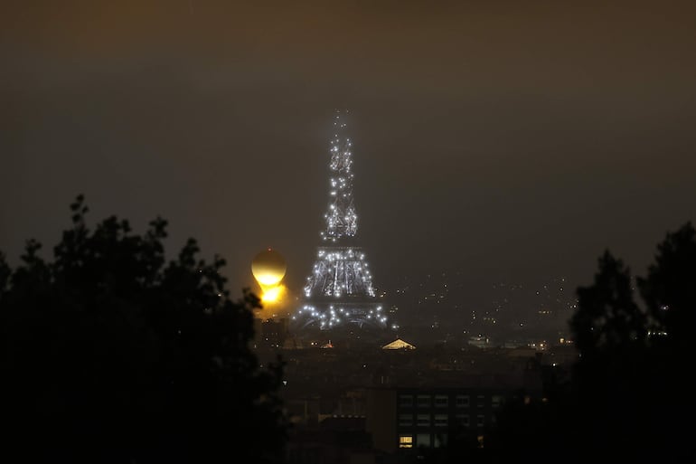 Fotografía del pebetero mientras se eleva en el aire enganchado a un globo aerostático junto a la Torre Eiffel durante la ceremonia de inauguración de los Juegos Olímpicos de París 2024.
