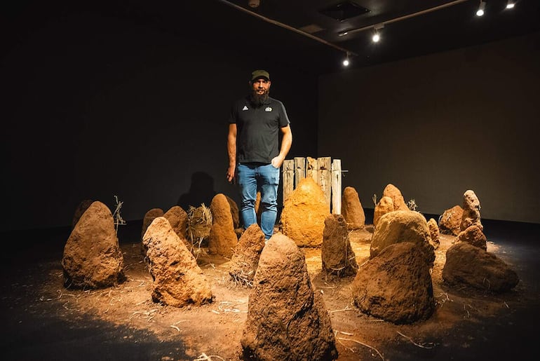 El artista Fidel Fernández posa con su instalación de takuru en el marco de la muestra "Cuadernos de campo", que fue adjudicada con el Premio AICA 2023.