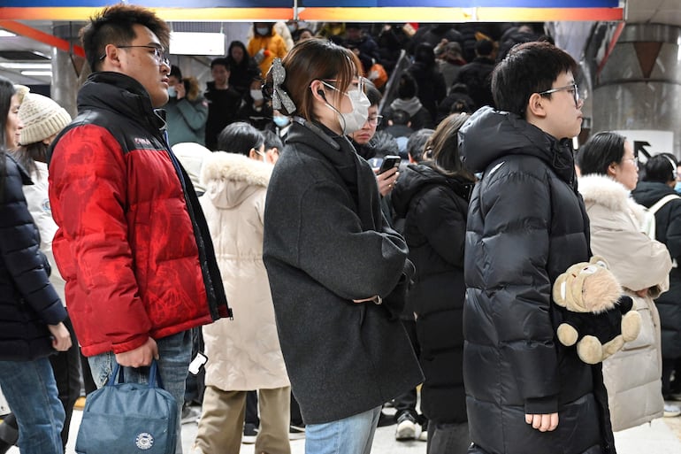 Zhang Yachun (derecha) llevando su robot impulsado por inteligencia artificial llamado Aluo mientras hace fila para tomar el metro en Pekín.
