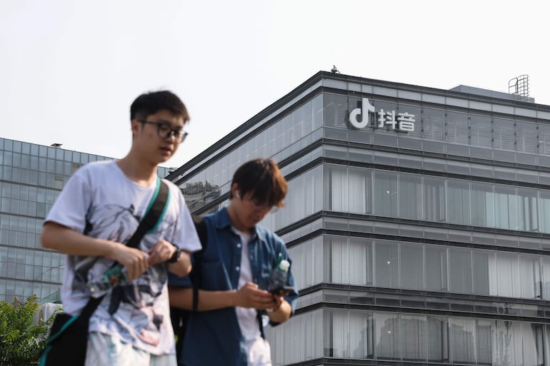 Dos jóvenes caminan frente a las oficinas de ByteDance, matriz de TikTok, en Pekín (China). No está muerto quien pelea, y parece que TikTok la va a luchar ante la intención de EE.UU. de prohibir la aplicación. Venía amenzando con hacerlo y lo hizo: demandaron ante un tribunal del distrito de Columbia la ley que pasó el Senado estadounidense semanas atrás.