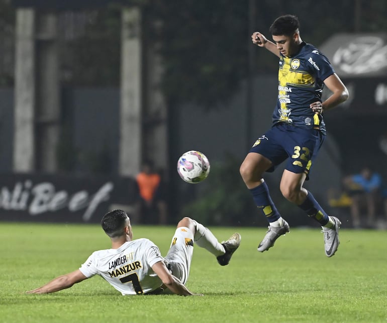 El jugador de Trinidense. Cristhian Martínez, salta para eludir la barrida del volante de Guaraní Agustín Manzur.