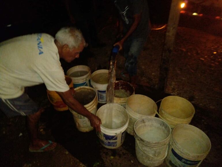 Un señor llena sus baldes de agua por la noche, horario en el que acudió el camión de la Essap a auxiliar a vecinos del bañado, que están teniendo problemas en la provisión del vital líquido.