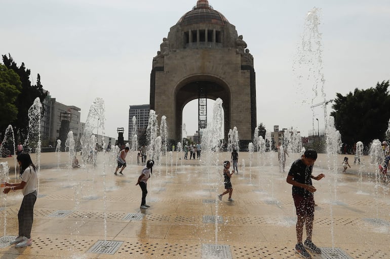 Personas juegan en una fuente del Monumento a la Revolución en la Ciudad de México (México). La onda de calor que azota desde hace 10 días a México cederá este domingo con lluvias en el sur, centro y norte del territorio, pero habrá temperaturas mayores a 40 grados en 14 estados del país, más de un tercio de los 32, según informó el Servicio Meteorológico Nacional (SMN).