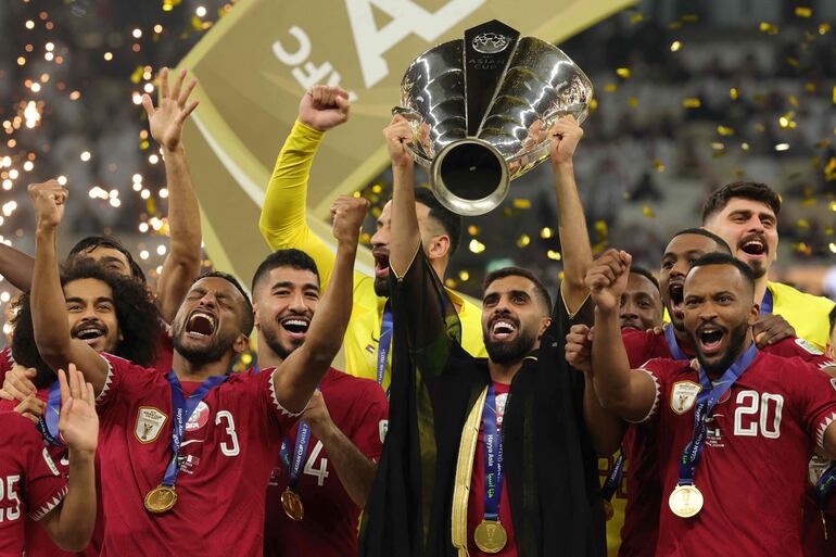 Qatar's forward #10 Hassan Al-Haydos lifts the Qatar 2023 AFC Asian Cup trophy as his team celebrates during the podium ceremony after the final football match between Jordan and Qatar at the Lusail Stadium in Lusail, north of Doha on February 10, 2024. (Photo by Giuseppe CACACE / AFP)