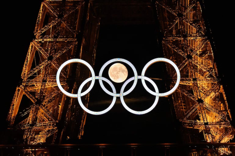 La Luna llena al fondo de la torre Eiffel y los aros olímpicos.