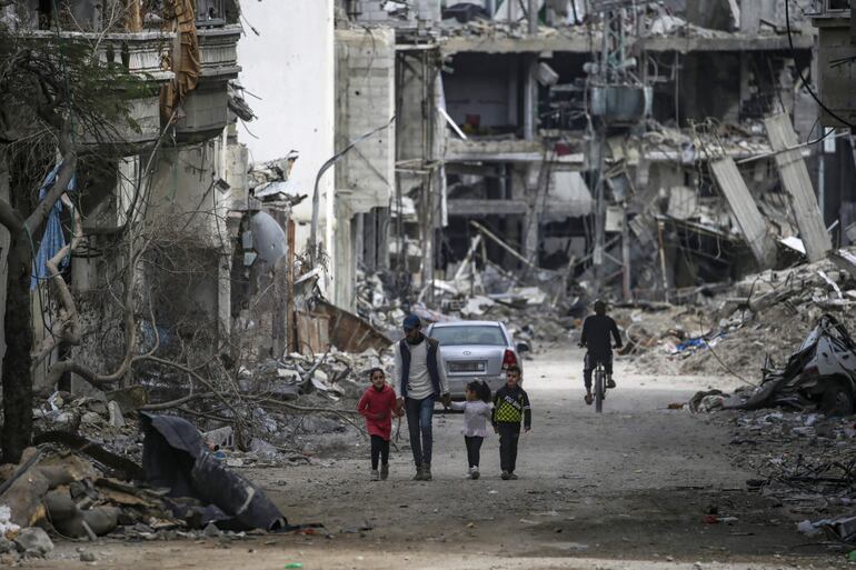 Una familia palestina camina entre la destrucción en el campo de refugiados de Al Bureije (Gaza). La ciudad gazatí de Rafah, donde se encuentra la mayoría de los casi dos millones de desplazados por la guerra, recibió fuego de artillería del Ejército israelí este martes (EFE).