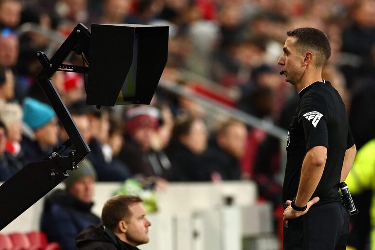 El árbitro inglés David Coote (R) consulta el monitor del campo antes de mostrar una tarjeta roja al defensor inglés de Brentford #16 Ben Mee después de que una revisión del VAR (árbitro asistente de video) aconsejara una mejora en su tarjeta amarilla durante el partido de fútbol de la Premier League inglesa entre Brentford y Aston Villa en el Gtech Community Stadium de Londres el 17 de diciembre de 2023.