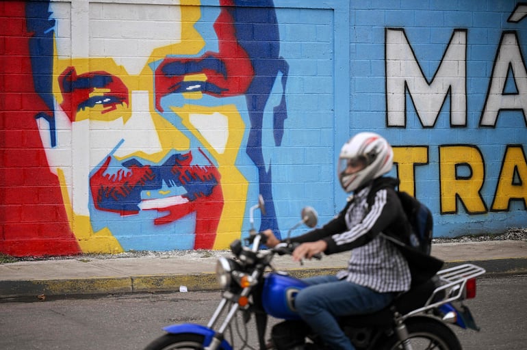 Un motociclista pasa junto a un mural del presidente y candidato presidencial venezolano, Nicolás Maduro, en Caracas el 23 de julio de 2024.