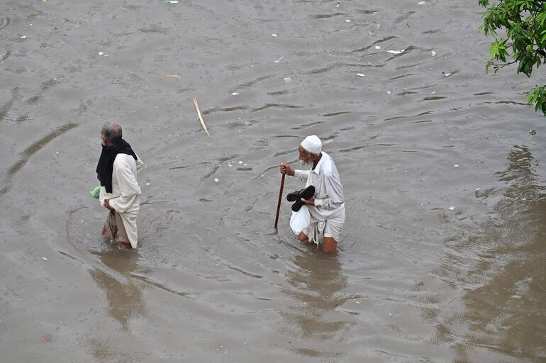 La gente se abre paso a través de un área inundada tras las fuertes lluvias en Lahore, Pakistán.