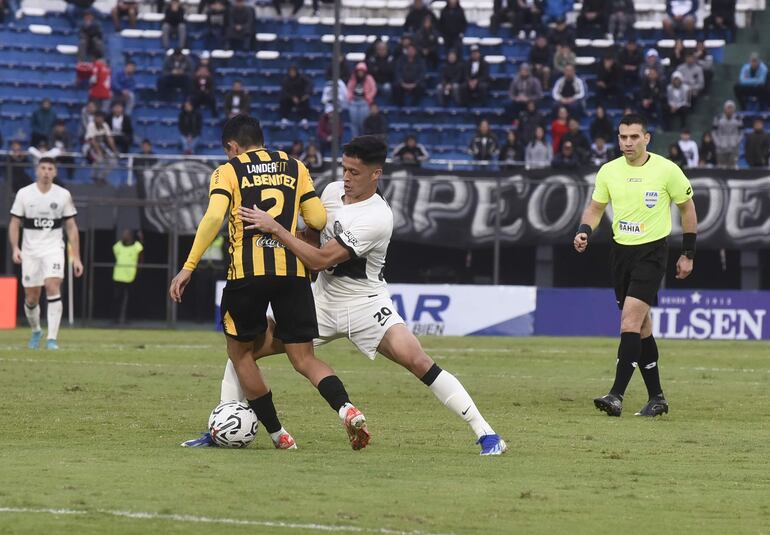 El volante de Olimpia, Alex Franco, pone freno al avance ofensivo del lateral de Guaraní Alcides Benítez.