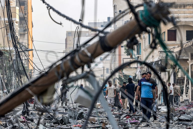 Varias personas caminan en una calle repleta de escombros luego de un bombardeo israelí en la Ciudad de Gaza, este miércoles.