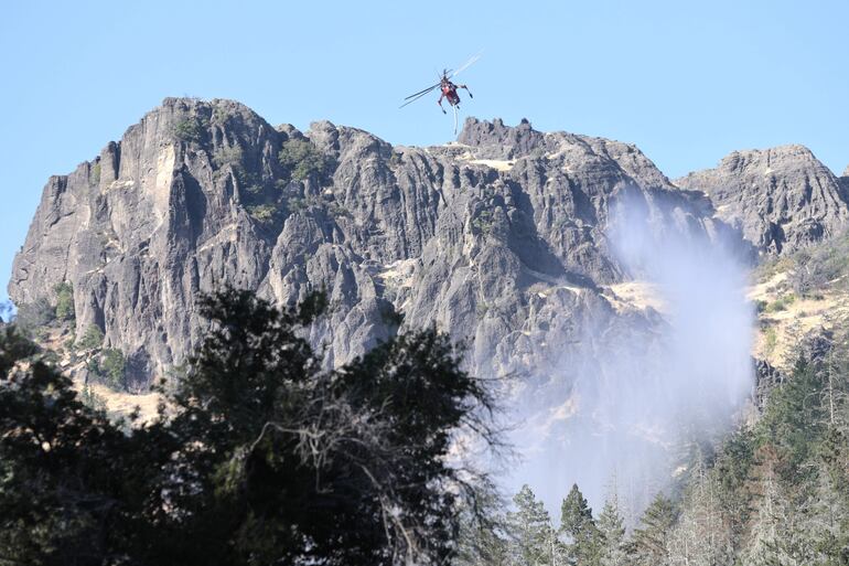 Un helicóptero deja caer agua en puntos calientes a lo largo de terreno empinado desde el incendio de peaje cerca de Calistoga en el condado de Napa, California.