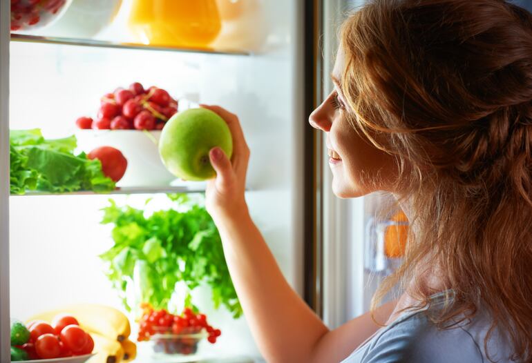 Mujer toma una manzana de la heladera.