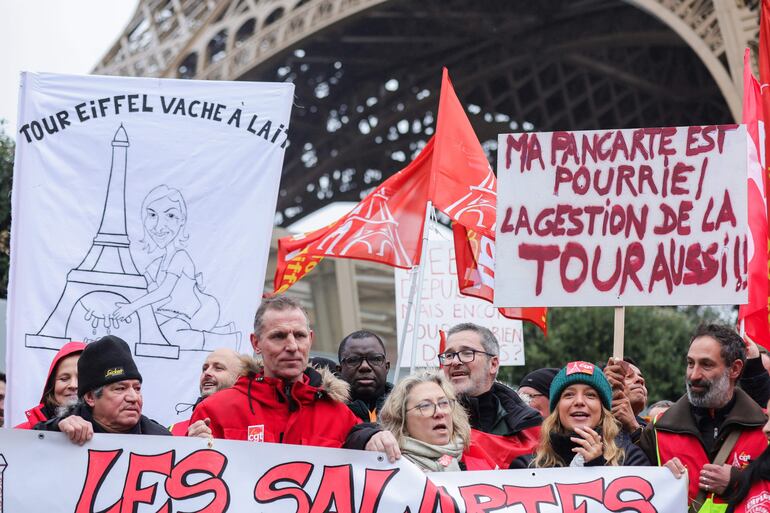 Los trabajadores en huelga llevan pancartas con los mensajes 'vaca lechera de la Torre Eiffel' (L) y 'mi pancarta es mala, también lo es la dirección de la torre' (R) durante una manifestación en Al pie de la Torre Eiffel en París.