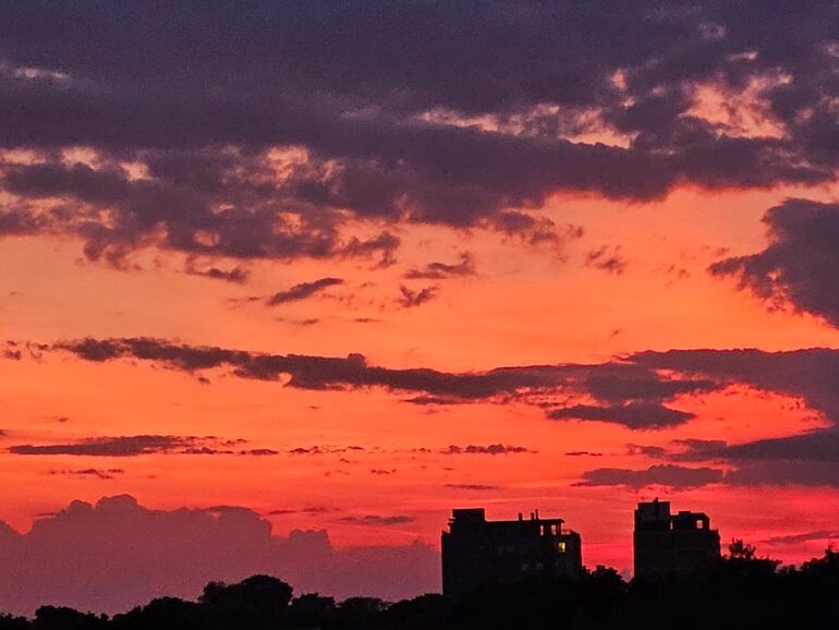 Cielo nublado con fondo de colores anaranjados y rosados, sobre dos edificios de altura a la distancia.