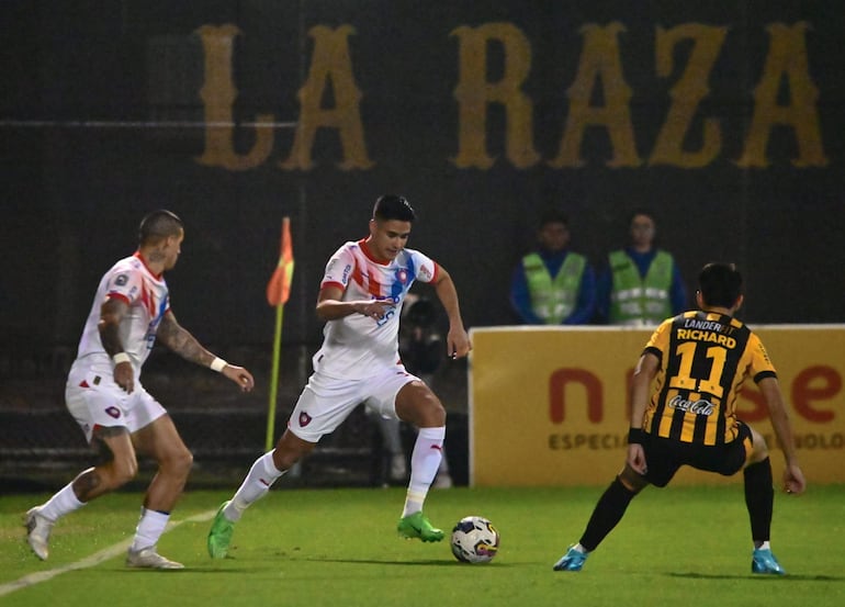 Rodrigo Melgarejo sale con la pelota ante la marca de Richard Prieto y la mirada de Alan Benítez