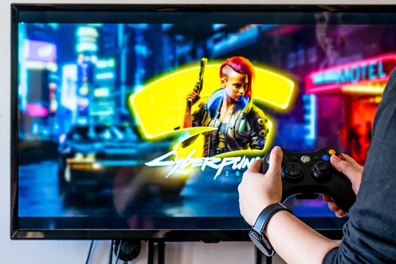 Mujer sostiene un control de Xbox y juega el popular videojuego Cyberpunk 2077.