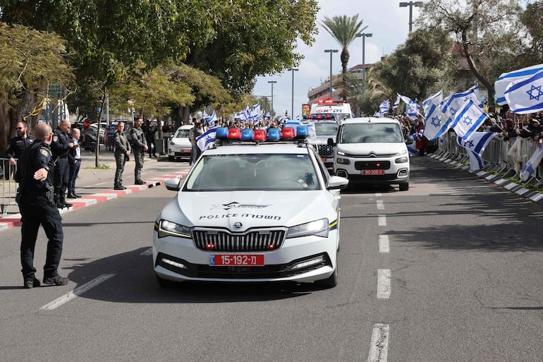 Los israelíes ondean la bandera nacional mientras el convoy de vehículos que transportan los cuerpos de los cuatro rehenes israelíes entregados por Hamás llega al Centro Nacional de Medicina Forense en Tel Aviv.