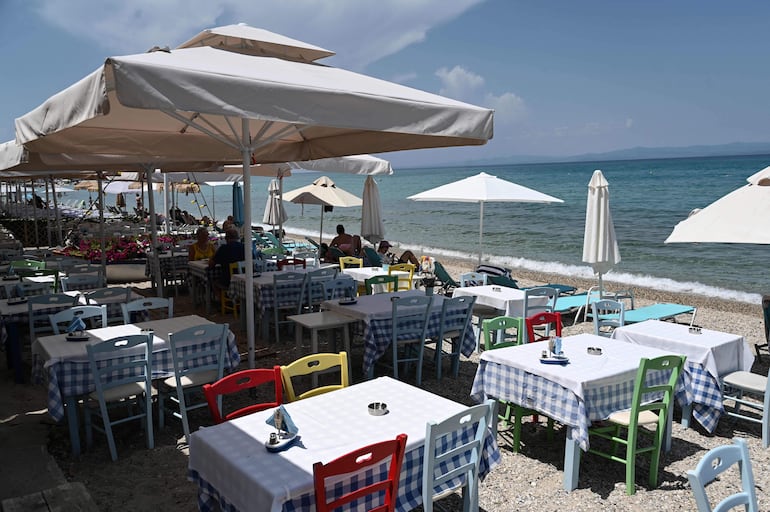 En una playa de la península griega de Calcídica, las olas del Egeo golpetean suavemente las mesas y sillas de dos restaurantes. La imagen es idílica, salvo que la situación es ilegal, porque los dos establecimientos carecen de licencia para ubicarse tan cerca del mar.