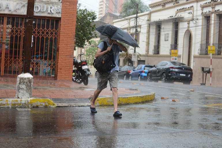 Un hombre se protege de la lluvia con un paraguas mientras cruza una calle en el microcentro de Asunción.