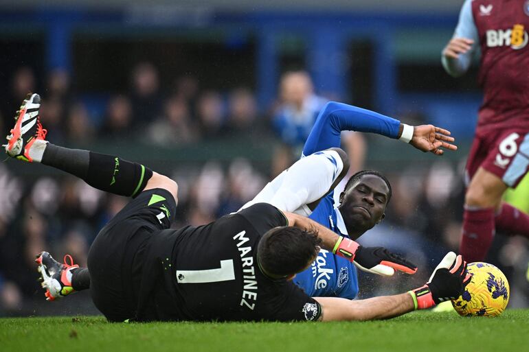 El portero argentino del Aston Villa #01 Emiliano Martínez (L) resulta herido mientras el centrocampista belga nacido en Senegal del Everton #08 Amadou Onana (R) se desliza para tratar de conseguir el balón regalando una falta durante el partido de fútbol de la Premier League inglesa entre Everton y Aston Villa en Goodison Park en Liverpool, noroeste de Inglaterra, el 14 de enero de 2024.