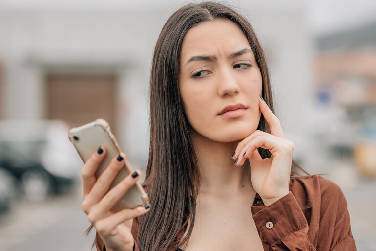 Una mujer mira con descofianza la pantalla de su teléfono celular.