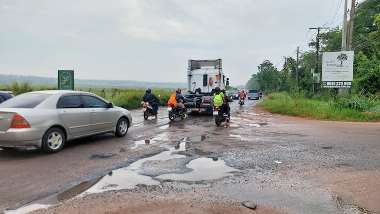 Motociclistas y automovilistas sortean un tramo lleno de baches y charcos en la ruta departamental D027, que cruza frente al Aeropuerto Internacional Silvio Pettirossi.