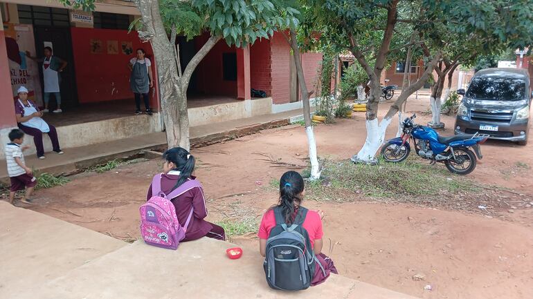 Dos alumnas almuerzan en el piso del patio, ante la mirada de las cocineras.