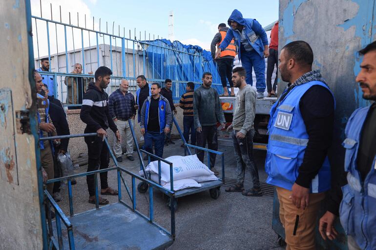 Miembros de la agencia de la ONU para refugiados palestinos distribuyen alimentos cerca de la puerta de Rafah, en Territorios Palestinos.  (AFP)