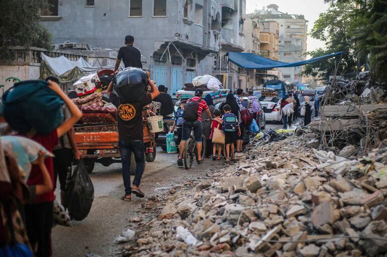 Los palestinos que transportan sus pertenencias personales huyen del campo de refugiados de al-Bureij en el centro de la Franja de Gaza. El ministro de Defensa israelí prometió el domingo golpear “con fuerza al enemigo” tras un bombardeo lanzado desde Líbano e imputado a Hezbolá que dejó 12 muertos en la zona anexada de los Altos del Golán, atizando el temor a una conflagración regional derivada de la guerra en Gaza.