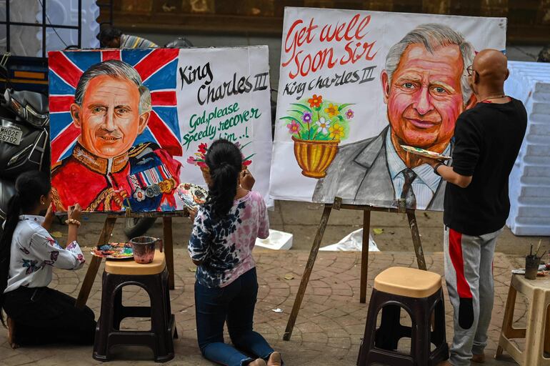 Un artista (derecha) y estudiantes dan los toques finales a las pinturas del rey Carlos III de Gran Bretaña para desearle una pronta recuperación, frente a una escuela de arte en Mumbai el 6 de febrero de 2024, tras el anuncio del Palacio de Buckingham sobre el diagnóstico de cáncer del monarca británico. (Punit PARANJPE / AFP)